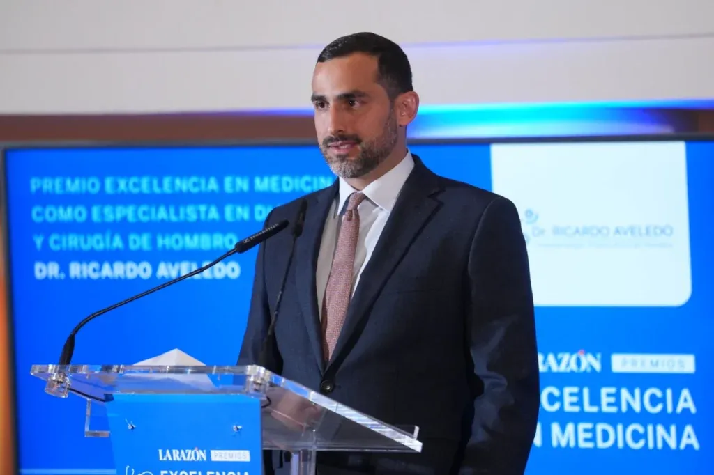 El Dr. Ricardo Aveledo interviene en la gala del Premio Excelencia en Medicina 2025; detrás, la pantalla anuncia su galardón como especialista en diagnóstico y cirugía de hombro