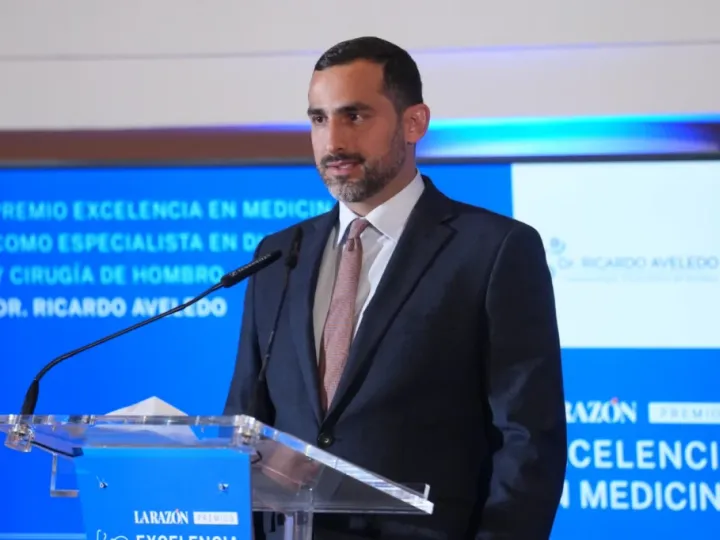 El Dr. Ricardo Aveledo interviene en la gala del Premio Excelencia en Medicina 2025; detrás, la pantalla anuncia su galardón como especialista en diagnóstico y cirugía de hombro
